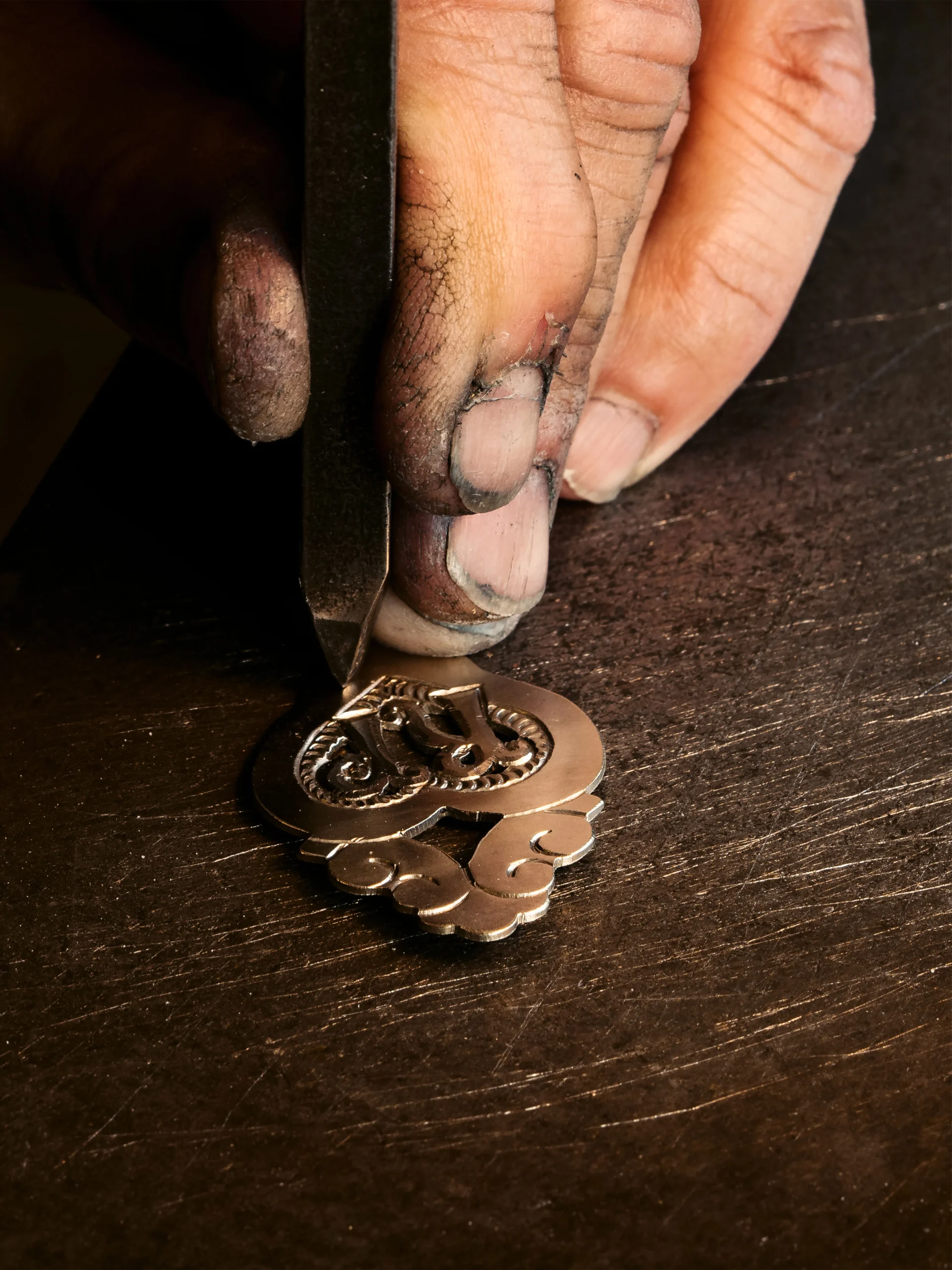 Appenzeller Kunsthandwerk von Hampi Fässler. Eine Hand die mit einem Meisel aus Metal eine Brosche herstellt.