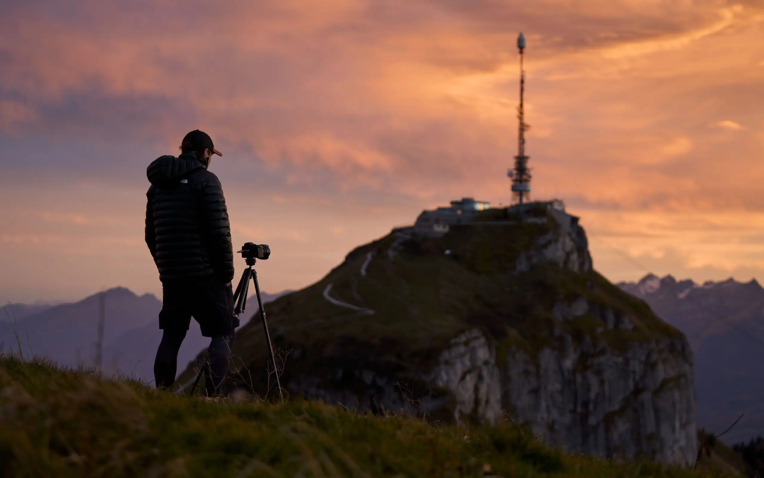 Fotograf mit Schirmmütze und mit Stativ, fotografiert die Bergstation auf dem Hohen Kasten in rotem Abendlicht.