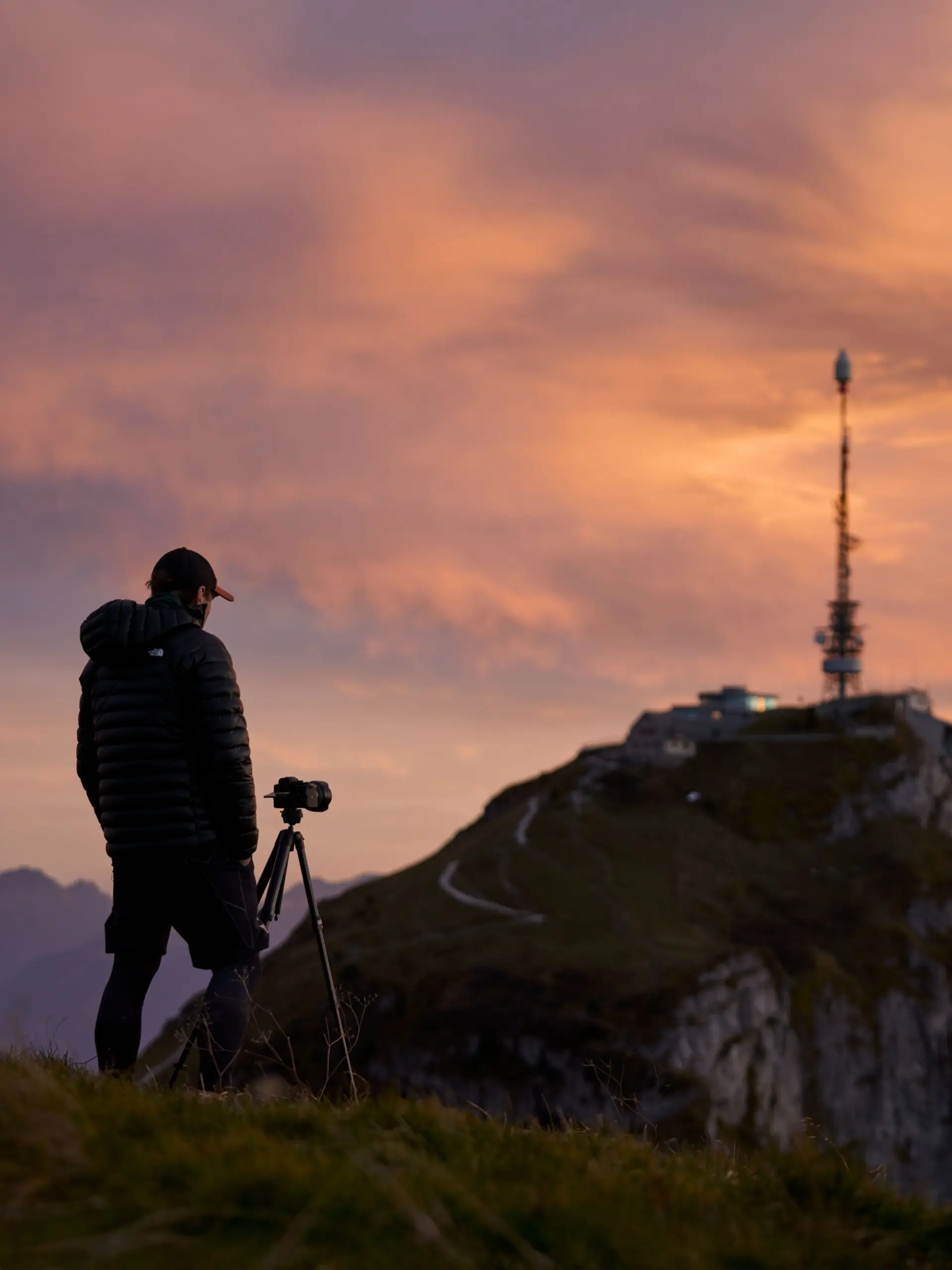 Fotograf mit Schirmmütze und mit Stativ, fotografiert die Bergstation auf dem Hohen Kasten in rotem Abendlicht.