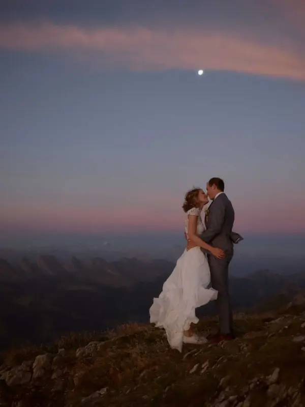 Brautpaar steht auf einem Berg bei Abendlicht auf dem Lisengrat, im Hintergrund der Mond und die Churfirsten.