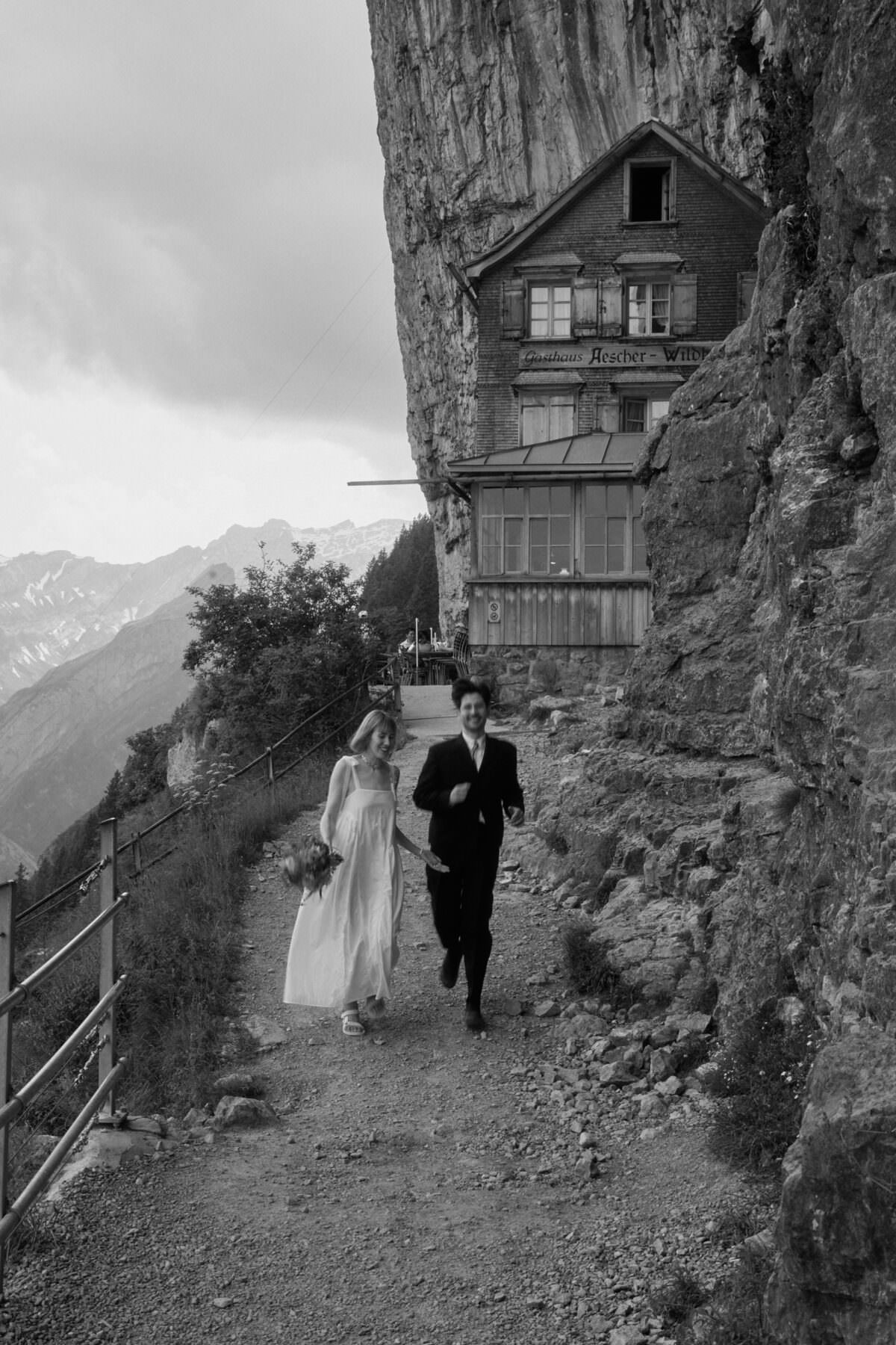 a groom and a bride running in front of aescher, an famous restaurant in appenzell