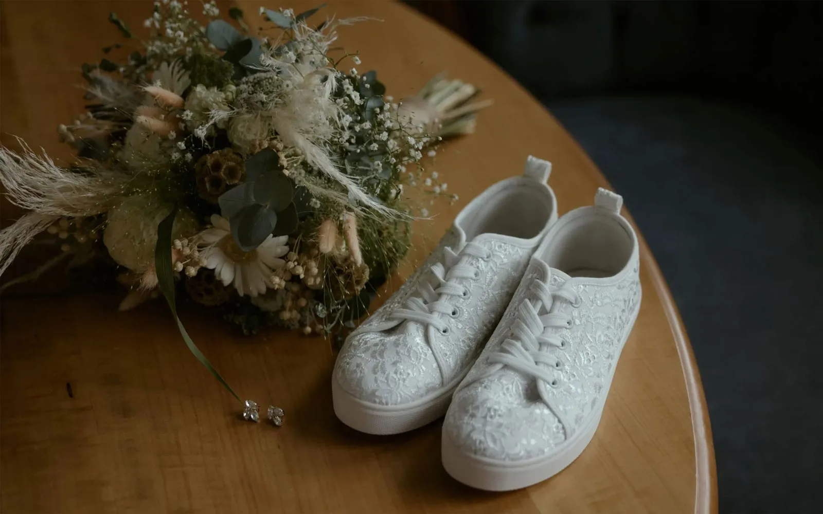 Weise Sneaker Schuhe einer Braut mit schönem Muster sind auf einem Tisch mit einem Blumenstrauss.