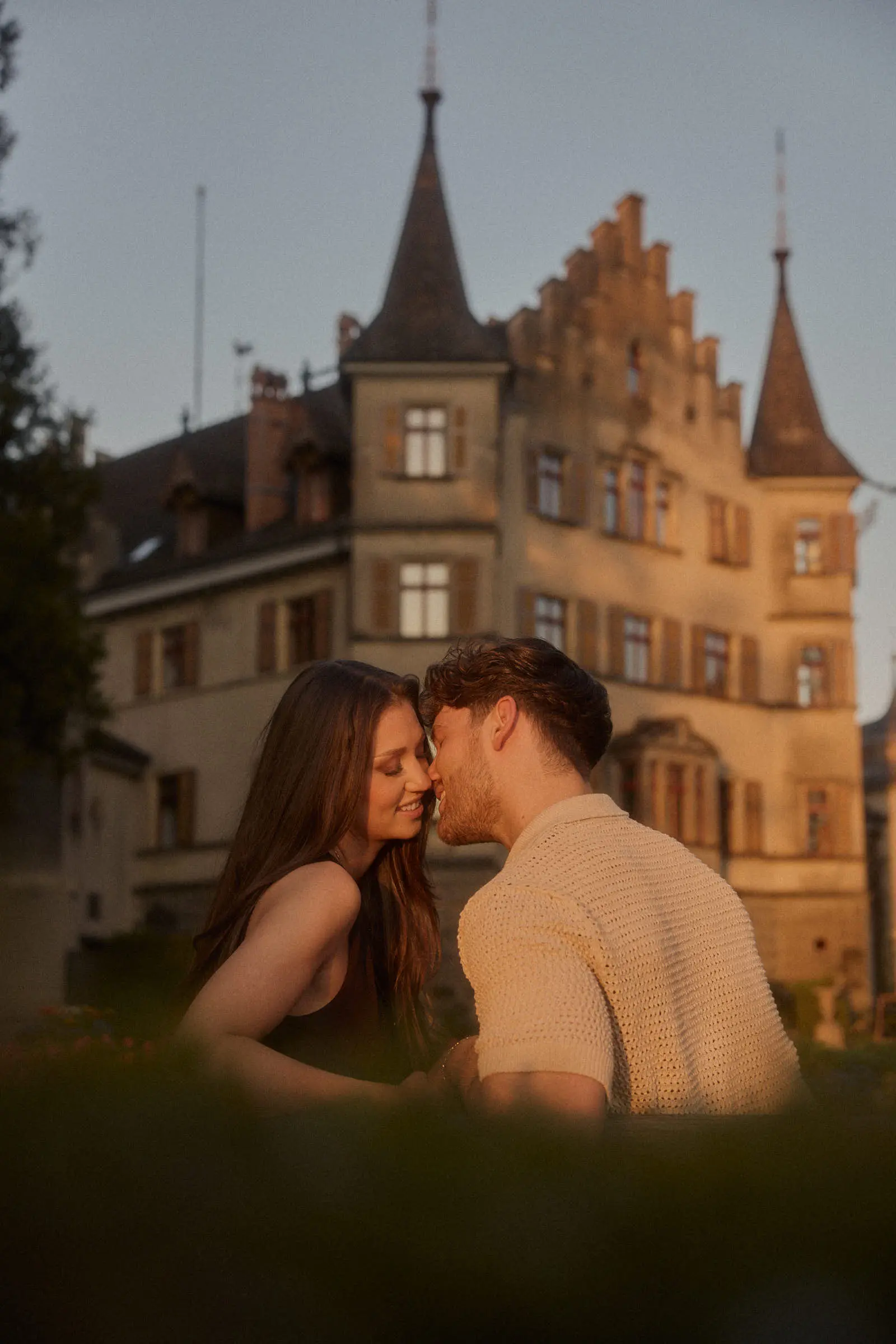 Paar küsst sich vor einem Schloss im Abendlicht