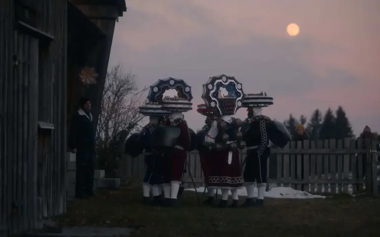 Silvesterchläuse mit kunstvollen Hauben in der Dämmerung bei Vollmond vor einem Bauernhaus in Hundwil, Appenzellerland