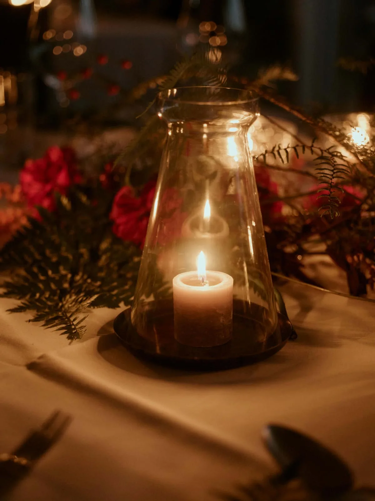 Candle lantern on a festive table with red flowers