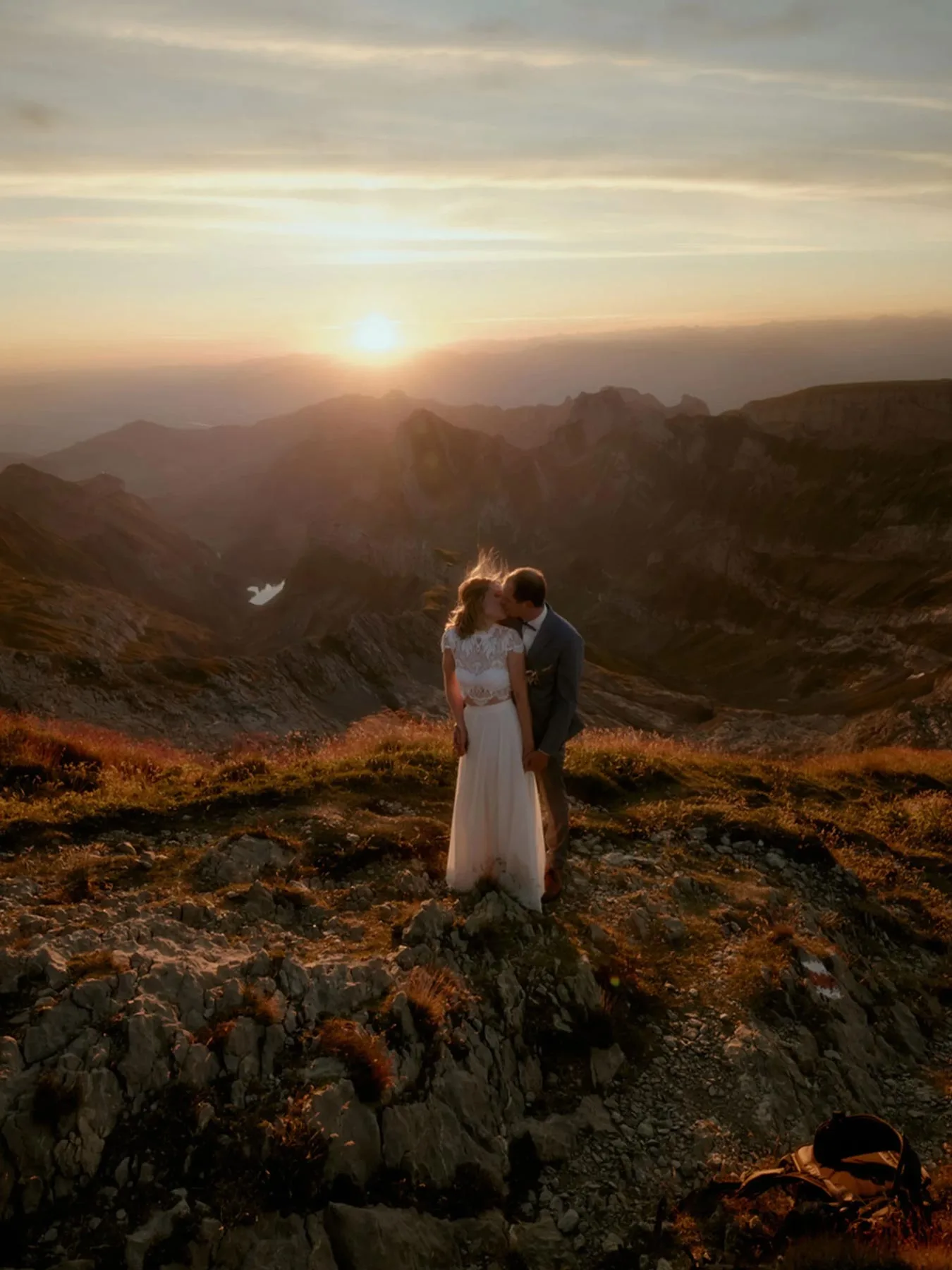 Eloping couple at sunset on a rocky ridge in the Alpstein, Switzerland, low sun over the peaks and a small lake below