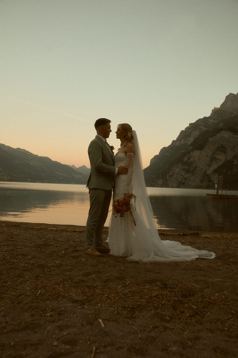 Bride and groom embracing at dusk on the shore of Lake Walen, Switzerland