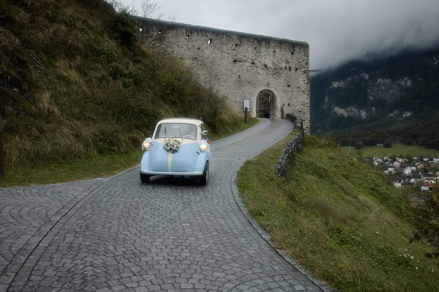 Kleines hellblaues Hochzeitsauto mit Blumenschmuck auf dem Pflasterweg zur Burg Gutenberg, Balzers