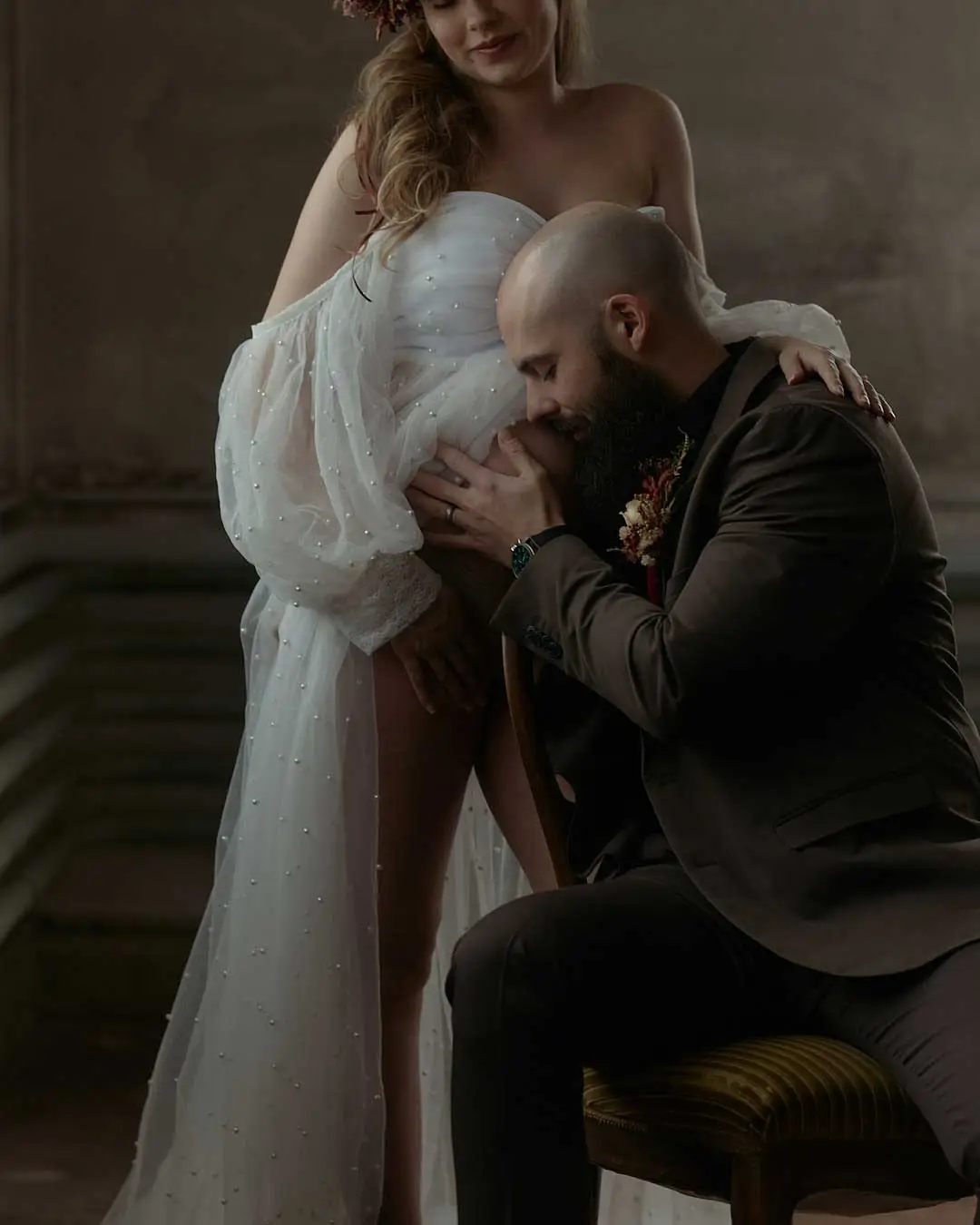 Man kissing the belly of a pregnant woman in a flowing white dress