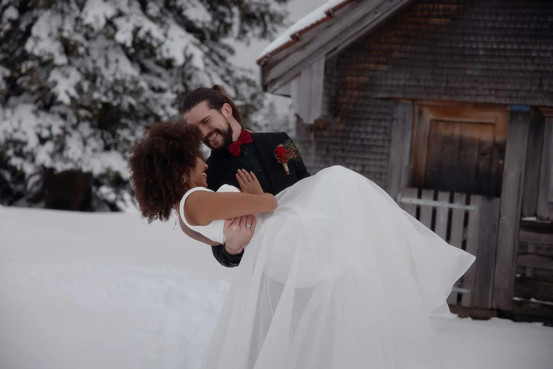 Bräutigam hebt die Braut im Schnee vor einer Alphütte, Winterhochzeit auf der Schwägalp